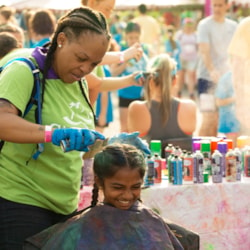 Girls on the Run volunteer spraying colorful hair spray in the hair of a participant